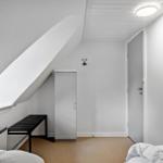 Zimmer mit schrägem Dach, Kleiderschrank, Bank und Bett.