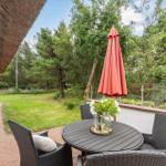 Terrasse mit Tisch, Stühlen und geschlossenem Sonnenschirm. Grünfläche und Bäume im Hintergrund.