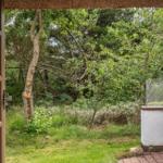 Durch offene Tür blickt man auf grünen Garten mit Bäumen und Sträuchern.