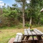 Holztisch mit Flasche und Gläsern auf Terrasse. Grün hinter dem Haus.