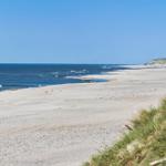 Weiterer Strandabschnitt mit Sand, Wasser und Dünen im Hintergrund.