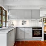 Küche mit grauen Schränken, weißer Arbeitsplatte und rotem Fliesenboden.