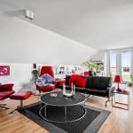 Wohnzimmer mit roten Sesseln, schwarzem Sofa und runden Tisch.