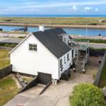 Wohnhaus mit Terrasse und Blick auf Wasser und Strand.