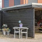 Außenbereich mit Tisch, zwei Stühlen und Pflanzen vor einem Holzschuppen.