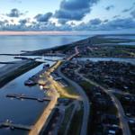 Aerial view of a coastal town at dusk with harbor, boats, and illuminated streets.