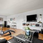 Wohnzimmer mit Fernseher, Glas-Tisch und Sitzgelegenheiten.