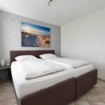 Schlafzimmer mit Doppelbett, Wandbild und Fenster mit Vorhang.