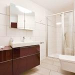 Badezimmer mit Dusche, Waschbecken und Toilette. Fliesenwand und dunkler Schrank.