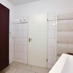 Badezimmer mit Dusche, Heizkörper und weißen Fliesen.