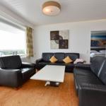 Wohnzimmer mit zwei schwarzen Sofas, Tisch und Blick auf Balkon.