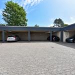 Garage mit mehreren Parkplätzen und gepflastertem Vorplatz unter blauem Himmel.