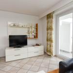Wohnzimmer mit TV, Schrank und Balkonzugang.
