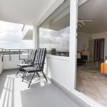 Terrasse mit zwei Stühlen und Blick auf Grünflächen. Durchgehende Glasschiebetüren führen ins Wohnzimmer.