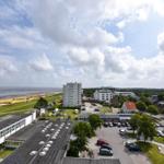 Blick auf Strand, Hotel und Parkplatz mit Bäumen und Autos.