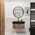 Badezimmer mit Holztür, runden Spiegel und schwarzer Waschbeckenkonsole.
