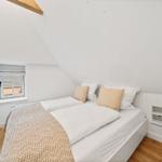 Schlafzimmer mit Dachschräge, Bett, Fenster und Fernseher an der Wand.