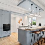 Küche mit grauen Schränken, Holzoberfläche und Barhocker.