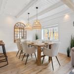 Essbereich mit Holztisch, Stühlen und Fenster. Küche mit Barhocker. Wohnbereich mit Sofa.