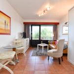 Wohnbereich mit Sofa, Sitzgruppe und Essplatz. Große Fensterfront mit Blick auf Balkon.