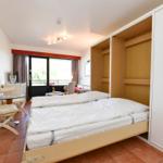 Schlafzimmer mit Bett, Kleiderschrank und Sitzbereich. Fenster mit Blick nach draußen.