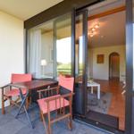 Terrasse mit Tisch und zwei Stühlen. Durch Glastür ist Wohnbereich sichtbar.