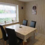 Esszimmer mit Tisch, vier Stühlen und Fenster. Wandbild und Blumen auf dem Fensterbrett.