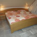 Schlafzimmer mit Doppelbett, Holzgestell und gemustertem Bettbezug.