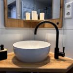 Waschbecken mit schwarzer Armatur auf Holzunterlage, Spiegel mit Holzrahmen und Kerzen.