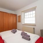 Schlafzimmer mit Bett, Kleiderschrank, Fenster und Sitzgelegenheit.