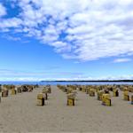 Strand mit gelben Strandkörben unter blauem Himmel mit Wolken.