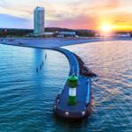 Hafenbecken mit Leuchtturm und Sonnenuntergang über Strand und Stadt.