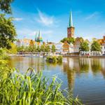 Hafenstadt mit historischen Gebäuden und grüner Ufervegetation unter blauem Himmel.