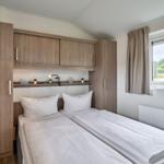 Zwei Betten mit weißen Bettwäschen, Holzschränke und Fenster mit Blick nach draußen.