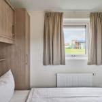 Schlafzimmer mit Bett, Schrank und Fenster mit Blick auf Grünfläche.