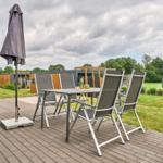 Terrasse mit Tisch, vier Stühlen und geschlossenem Sonnenschirm. Hintergrund: moderne Häuser und Grünfläche.
