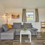 Wohnzimmer mit grauem Sofa, Tisch und Fenster.