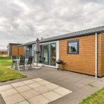 Moderne Holzhütte mit Terrasse, Grill und Garten. Glastüren führen ins Innere.