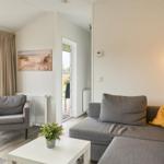 Wohnzimmer mit Sofa, Sessel und Tisch. Durchgang zu Terrasse und Garten.