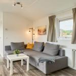 Wohnzimmer mit Sofa, Tisch und Fenster. Im Hintergrund ist das Schlafzimmer zu sehen.