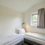 Zwei Einzelbetten mit weißen Bettwäschen, Fenster mit Vorhang und Wandlampe.