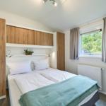 Schlafzimmer mit Doppelbett, Holzschränken und Fenster mit Blick auf Grün.