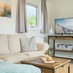 Wohnzimmer mit Sofa, Fernseher und Fenster. Auf dem Tisch steht eine Kerze.
