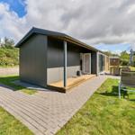 Moderne Hütte mit Terrasse und Gartenmöbeln. Grün umgeben mit Blick auf Wald.