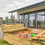 Außenbereich mit Sandkasten, Gartenmöbeln und Terrasse vor modernem Haus.