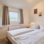 Schlafzimmer mit Doppelbett, Fenster und Wandbildern.