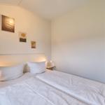 Schlafzimmer mit Doppelbett, Wandbildern und angrenzender Küche.