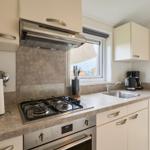 Küche mit Herd, Spüle und Fenster. Außenterrasse sichtbar.