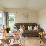 Wohn- und Essbereich mit Sofa, Tisch und Stühlen. Fenster mit Blick nach draußen.