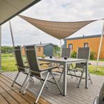 Terrasse mit Tisch, Stühlen und Sonnensegel. Hintergrund: Wohnmobile und Grünflächen.